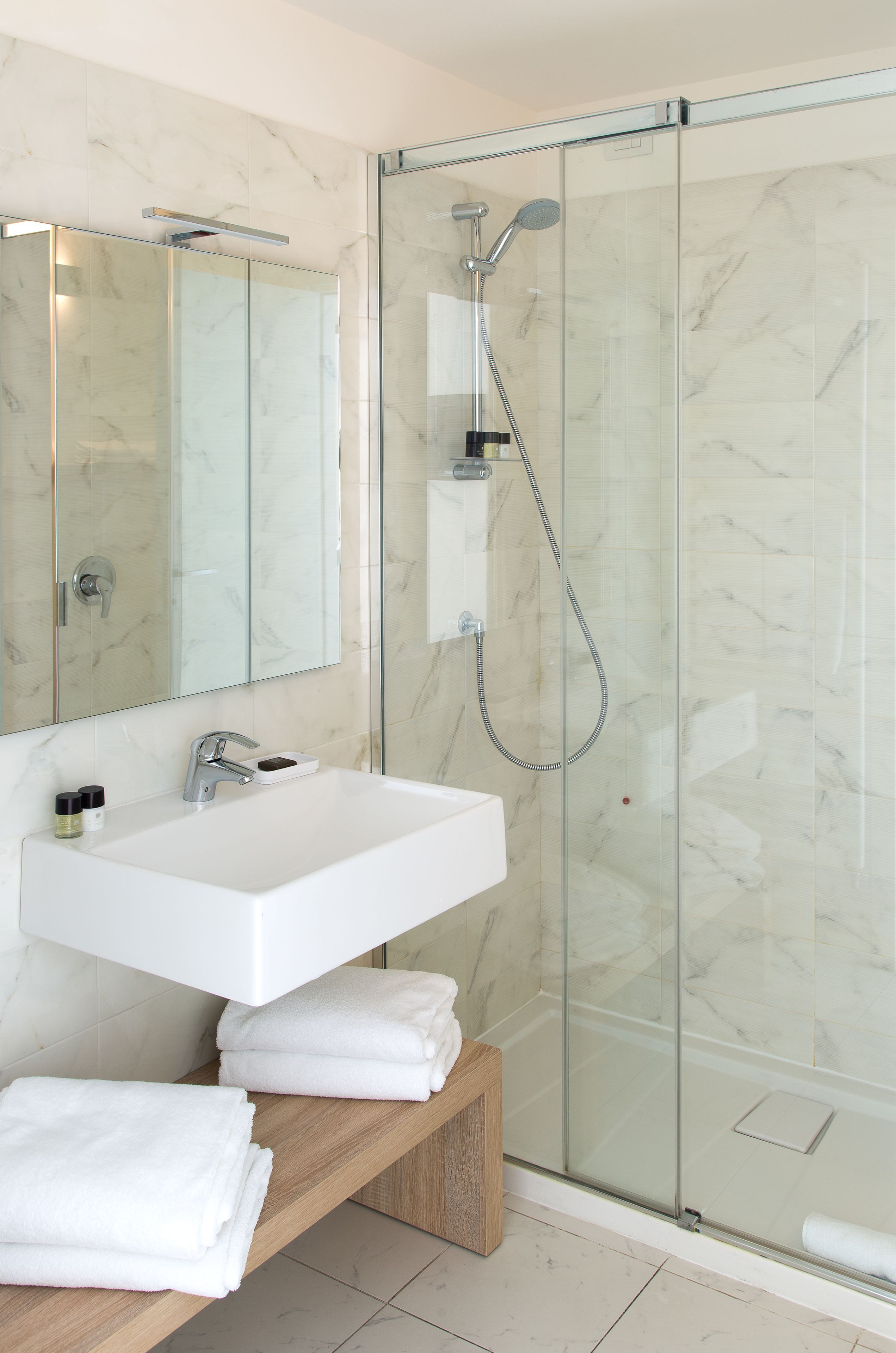 Un baño moderno con cabina de ducha acristalada, lavabo blanco y banco de madera.