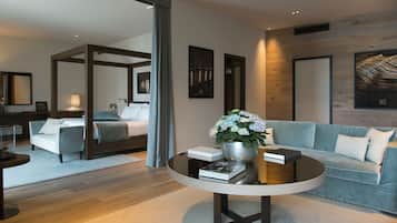 Una habitación de hotel moderna con una cama, un sofá, una mesita de centro con libros y un jarrón de flores, y un espejo grande.