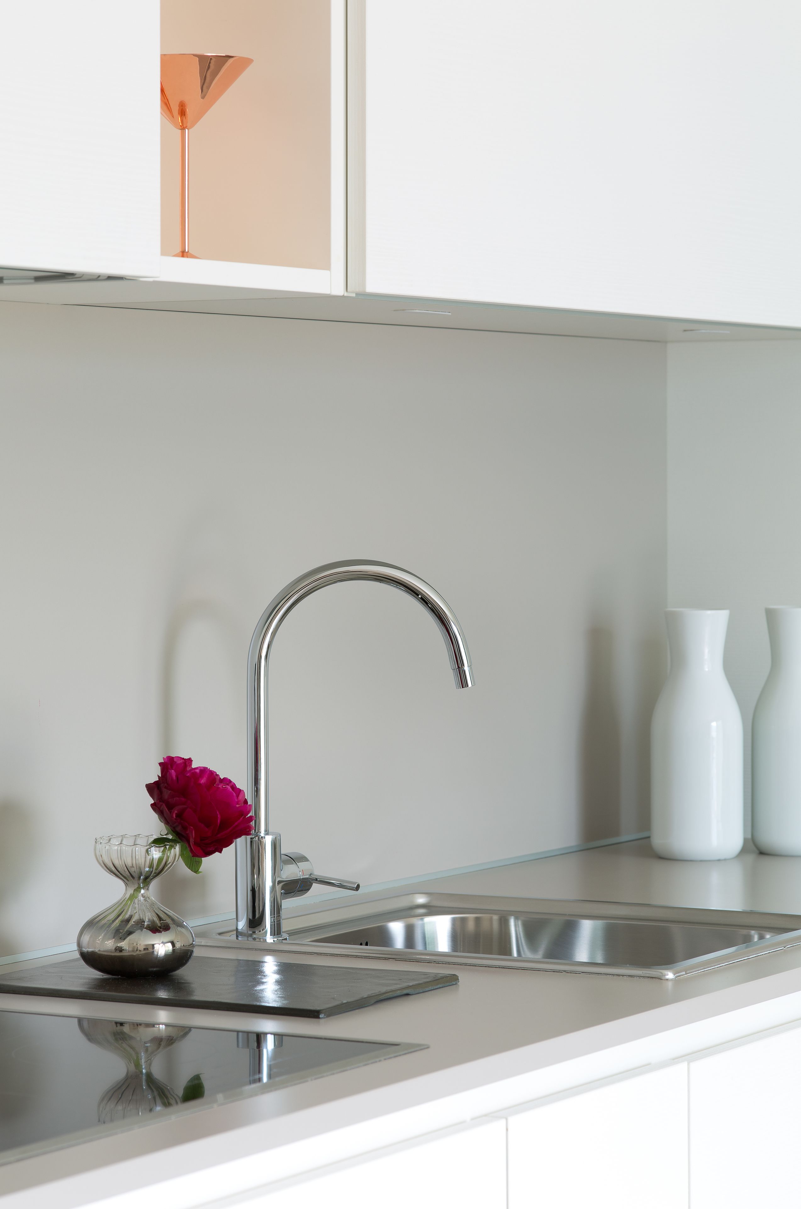 Una cocina moderna con un lavamanos de acero inoxidable, una rosa en un florero de vidrio y armarios blancos.