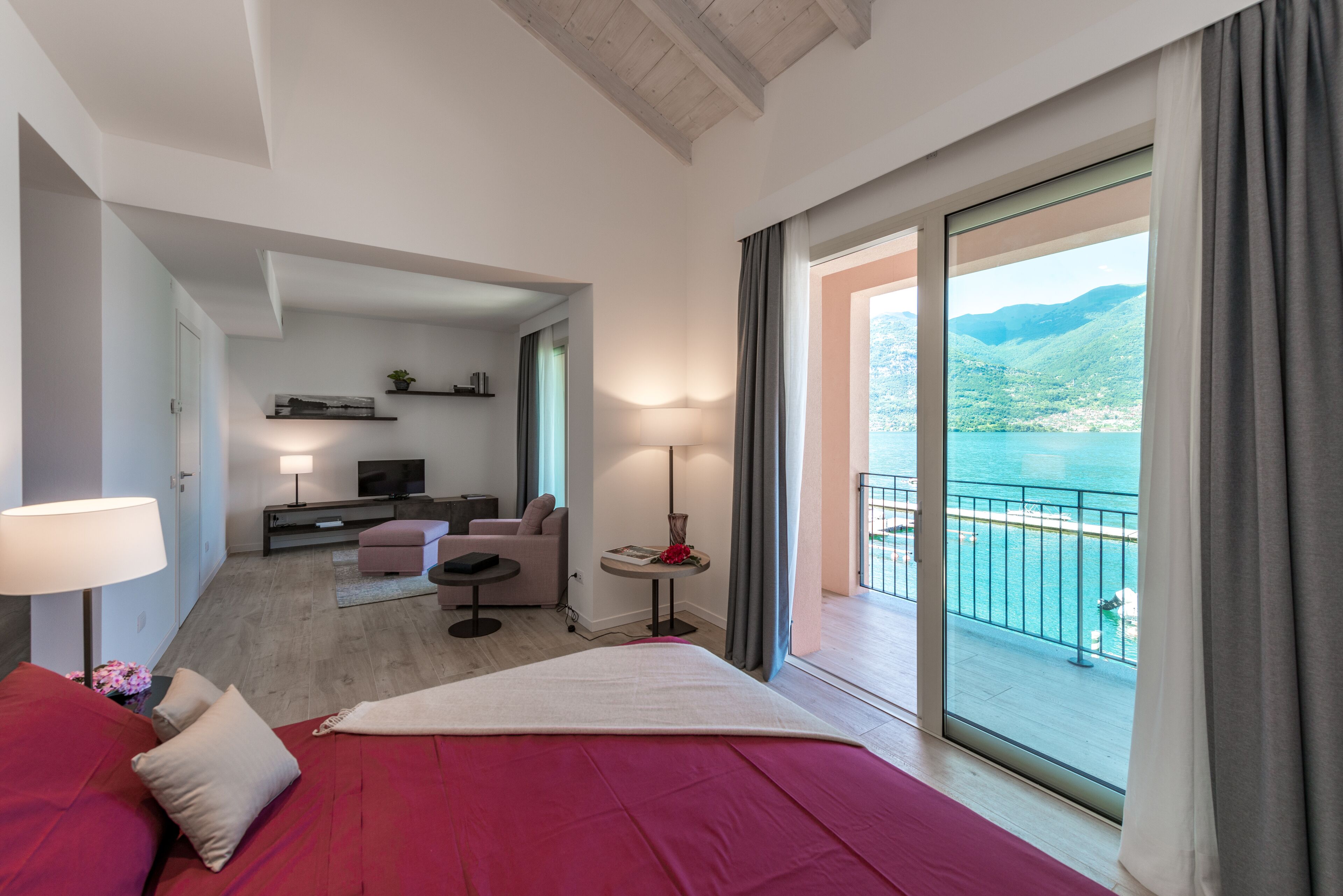 A hotel room with a bed, a desk, a sofa, and a balcony with a view of the sea and mountains.
