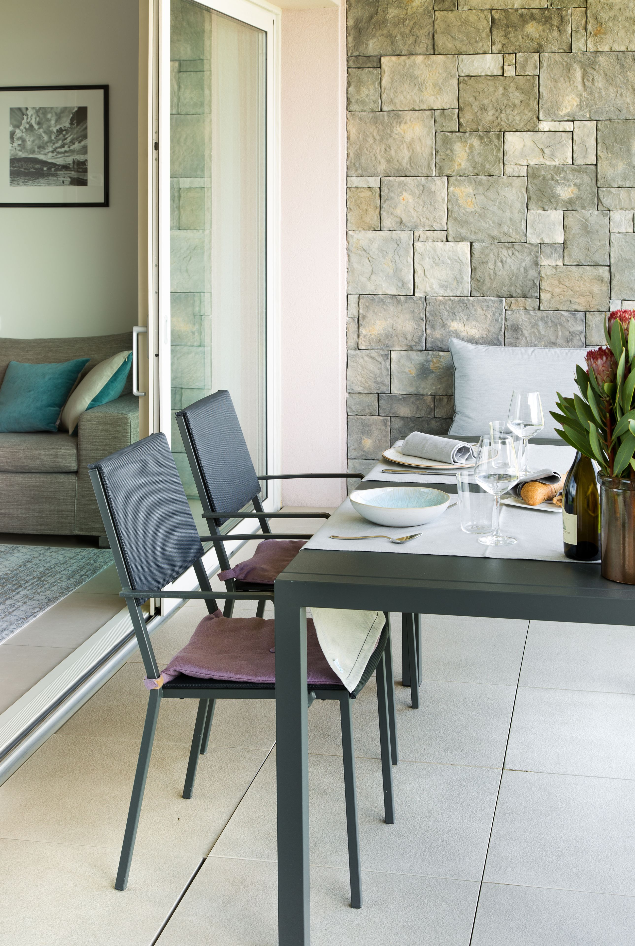 Un coin repas avec un mur en pierre, un canapé et une table dressée pour deux personnes, avec des chaises.