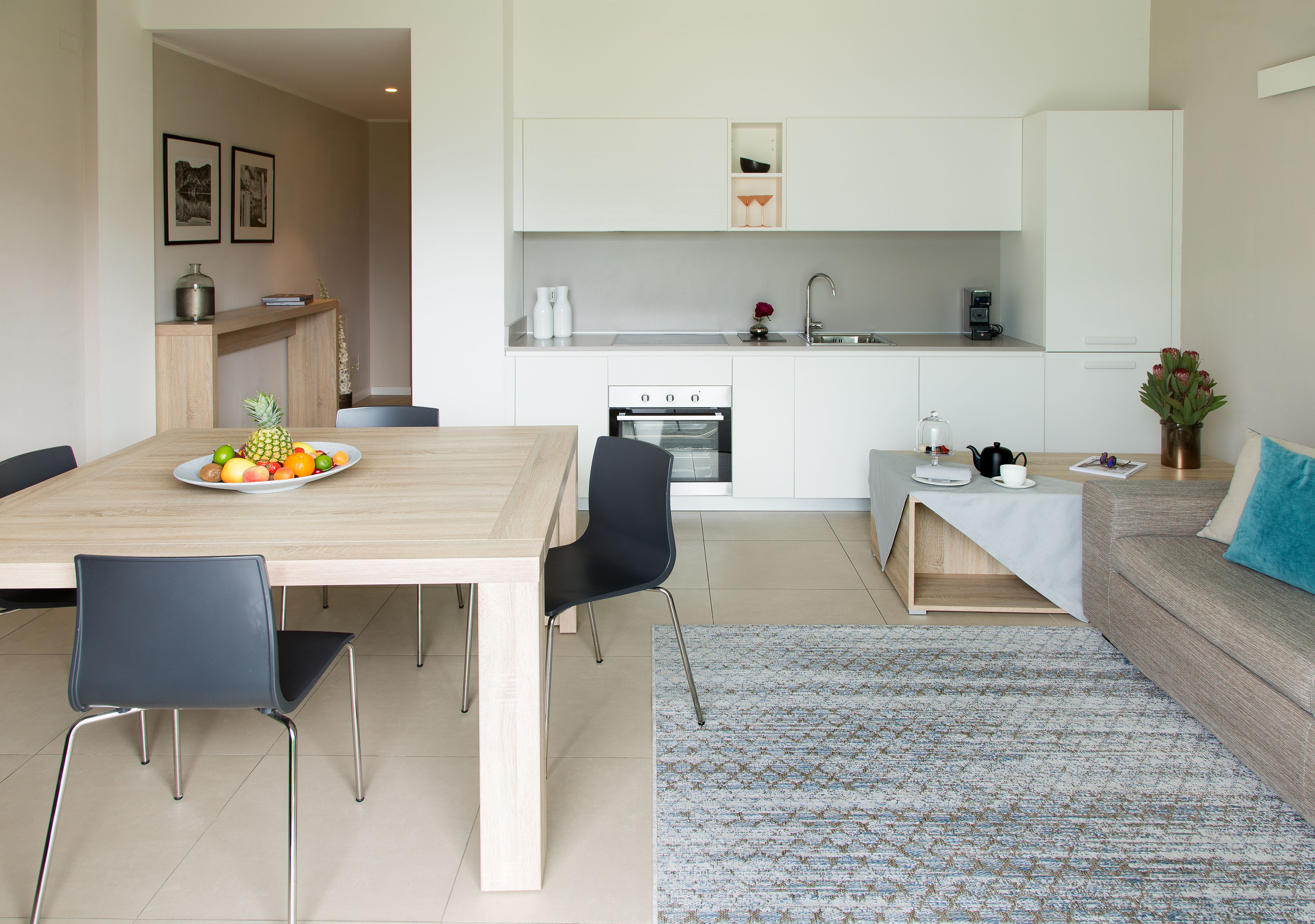 A modern kitchen with white cabinets, a built-in oven, and a dining area with a wooden table and chairs.