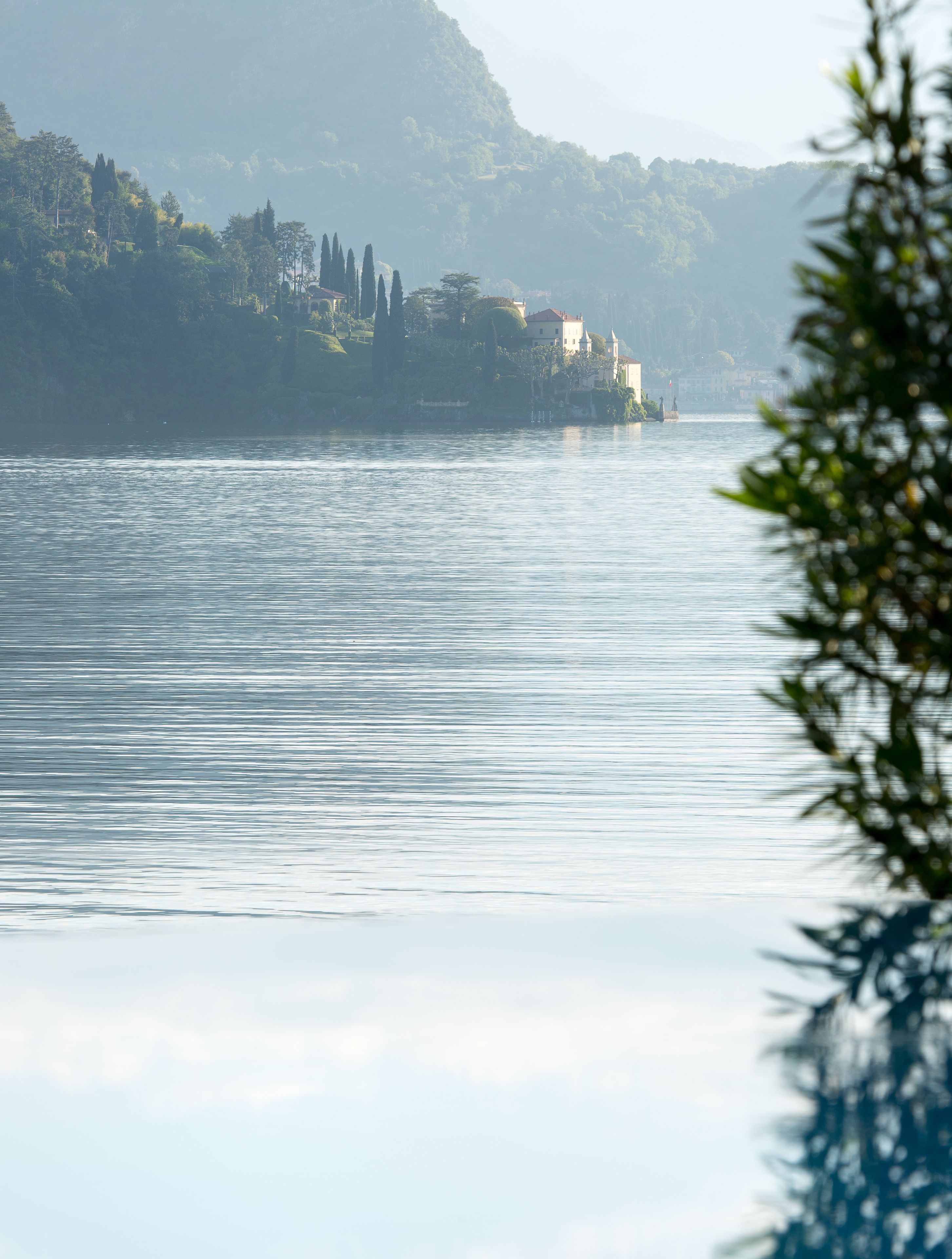 A calm lake with a mountain in the background and a building on the shore.