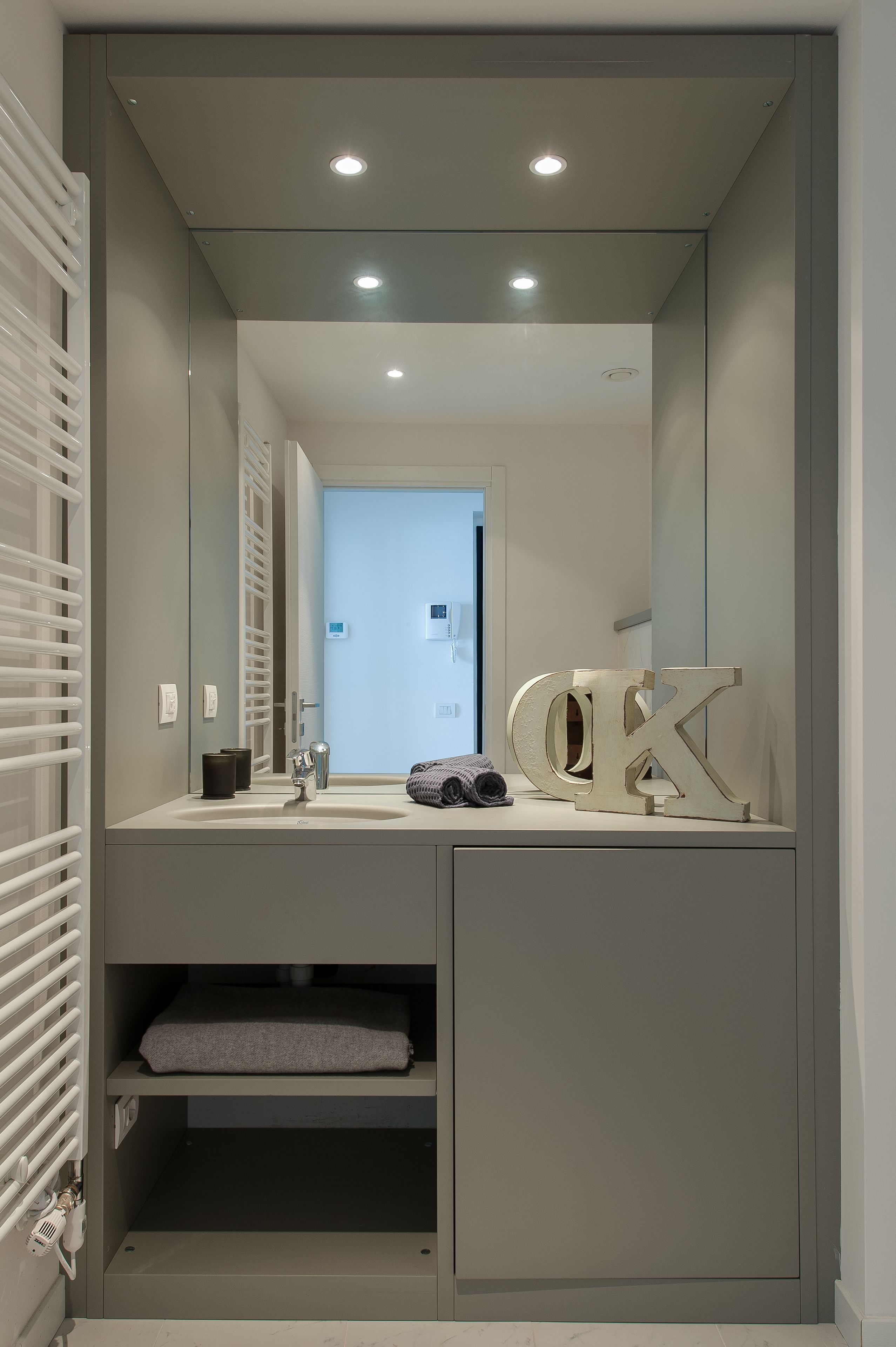 A modern bathroom with a large mirror, recessed ceiling lights, a towel rack, and a vanity with a sink.