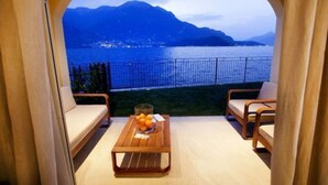 A balcony with a wooden table, two chairs, and a view of a lake and mountains.