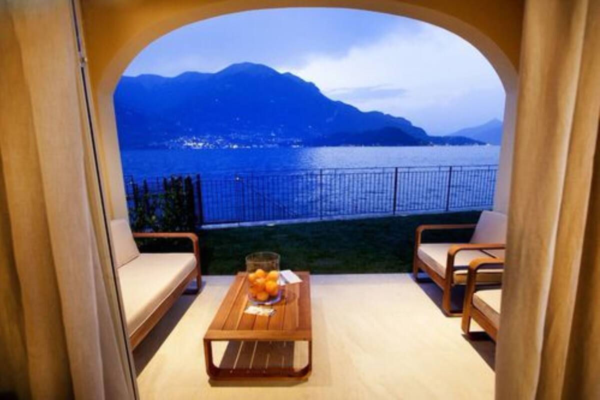 Een balkon met een houten tafel, twee stoelen en uitzicht op een meer en bergen.