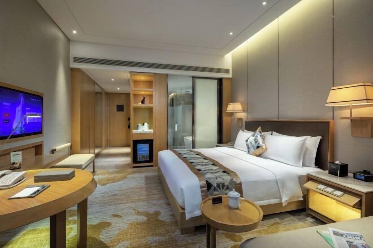 Une chambre d’hôtel moderne équipée d’un lit, de tables de chevet, d’un bureau, d’une télévision et d’un mini-bar.