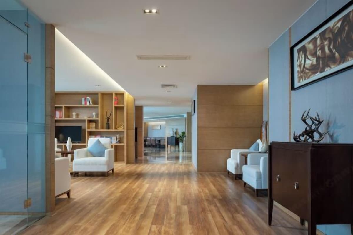 Un moderno vestíbulo de hotel con piso de madera, sofás blancos, un mueble de madera oscura y un cuadro abstracto grande en la pared.