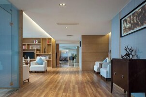 Un moderno vestíbulo de hotel con piso de madera, sofás blancos, un mueble de madera oscura y un cuadro abstracto grande en la pared.