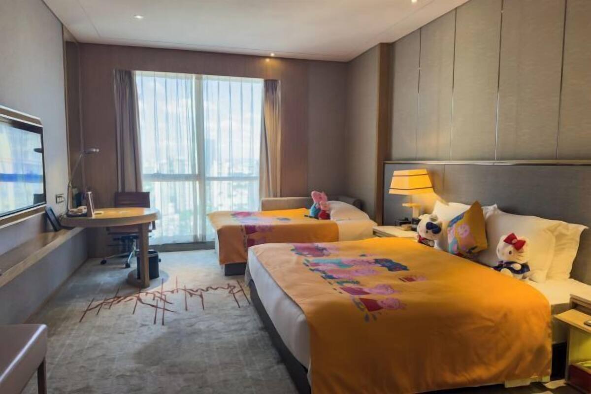 Une chambre d’hôtel avec deux lits, un bureau, une chaise, une télévision et une fenêtre avec des rideaux.