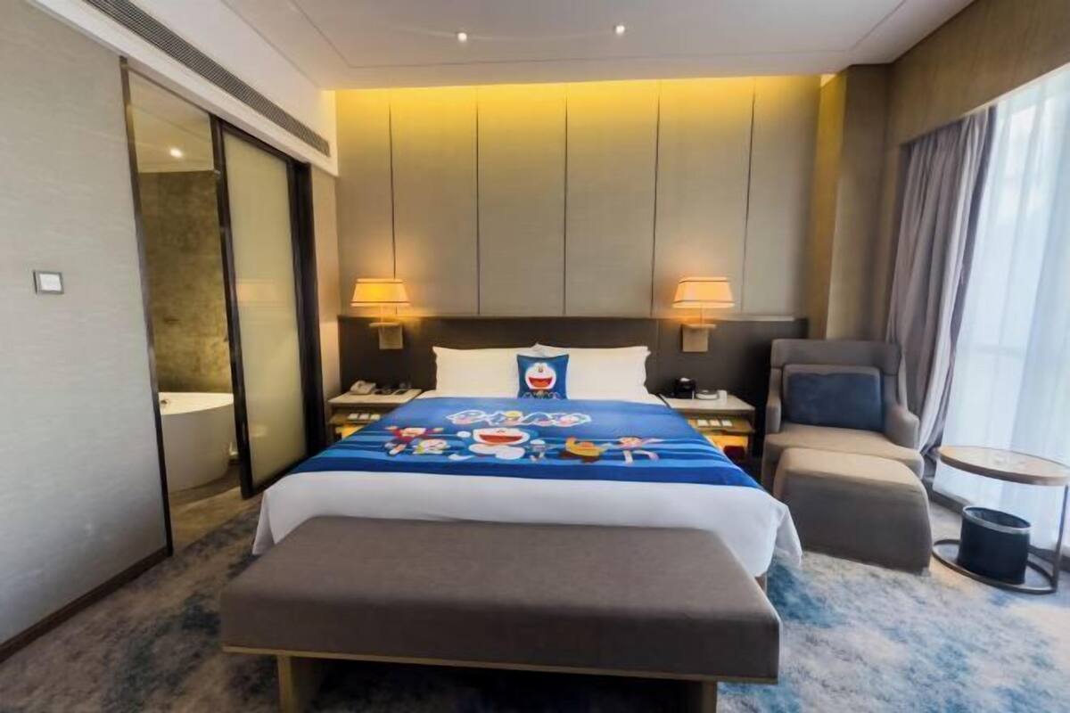 Une chambre d’hôtel avec un lit, des tables de chevet, une chaise, une petite table et une fenêtre.
