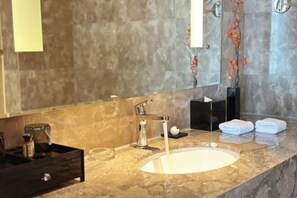 Un baño moderno con lavamanos de mármol, un espejo grande y un florero con flores.