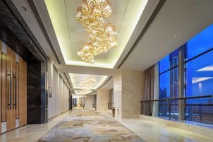 A hotel corridor with a marble floor, large windows, and a modern chandelier.