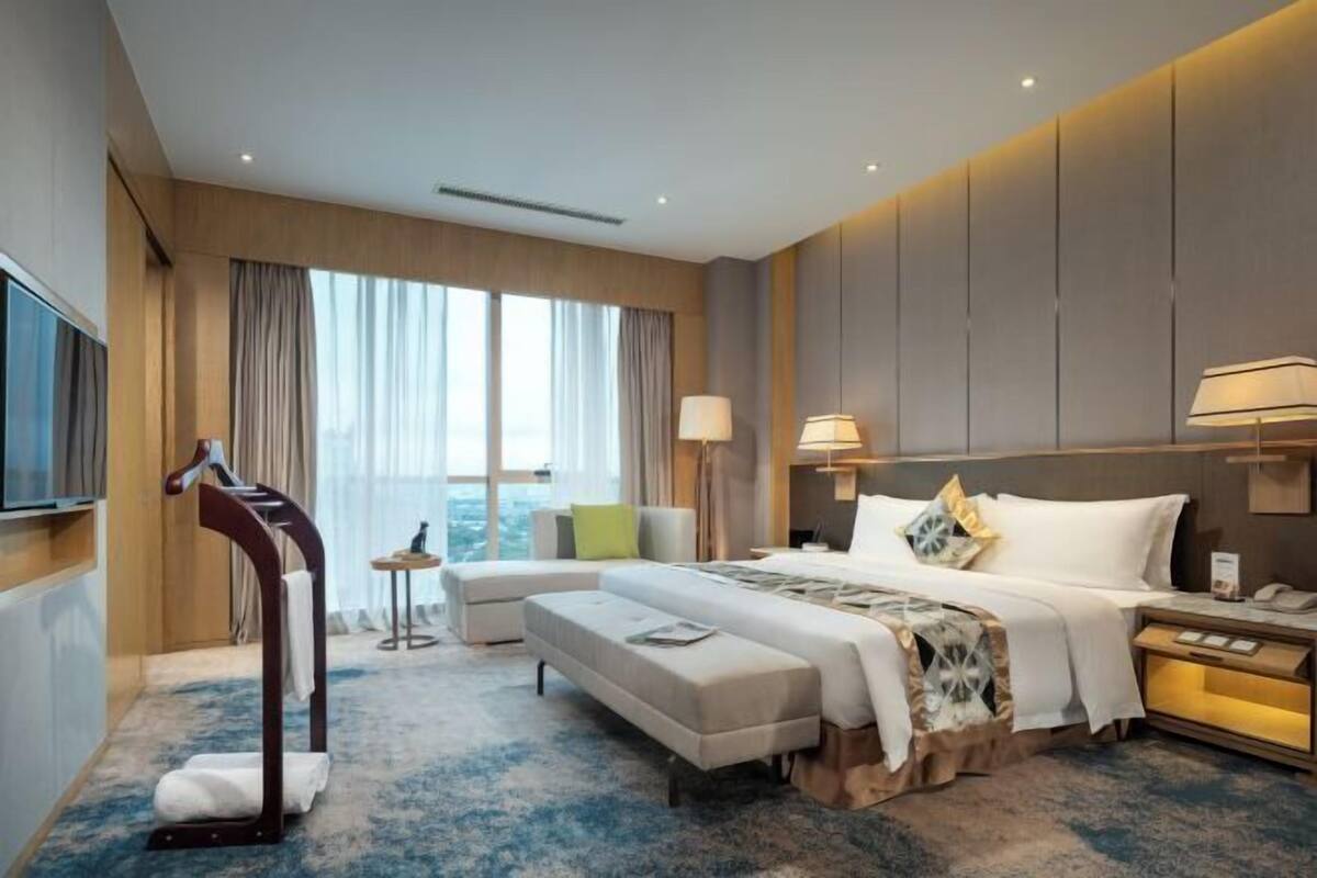 Une chambre d’hôtel avec un grand lit, un coin salon, une télévision et une fenêtre avec des rideaux.