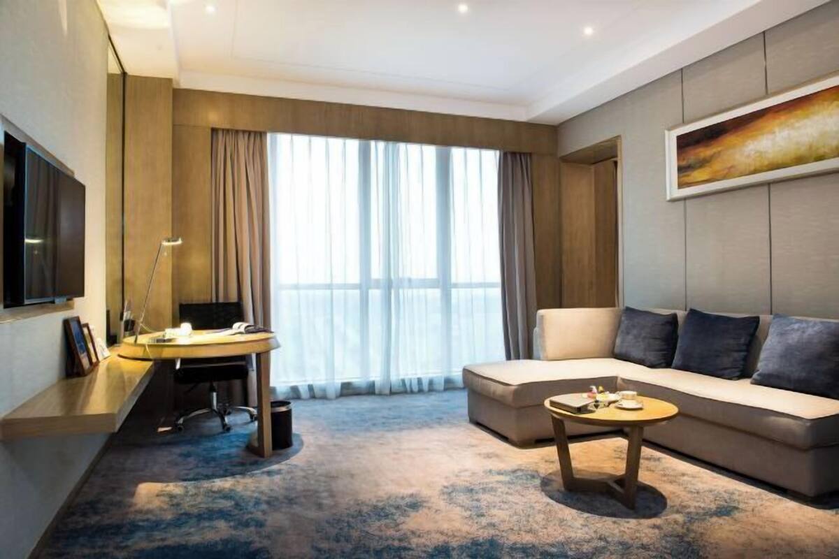 Une chambre d’hôtel moderne équipée d’un canapé, d’un bureau, d’une télévision et d’une grande fenêtre avec des rideaux.