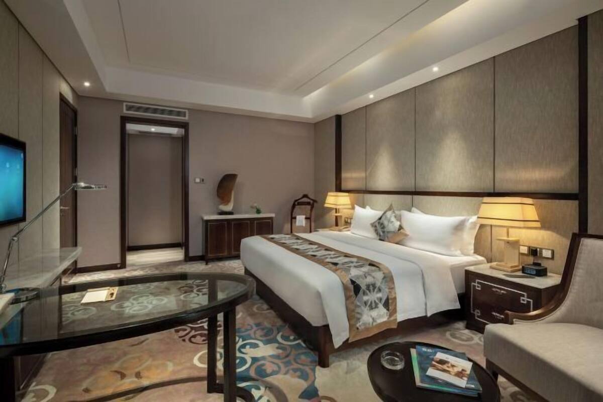 Une chambre d’hôtel comprenant un lit, des tables de chevet, un téléviseur, une table basse en verre et une chaise.