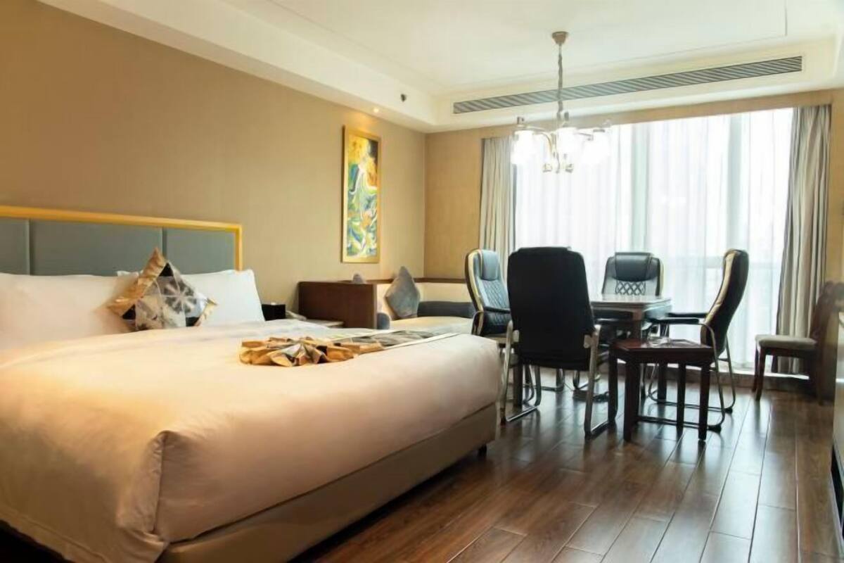 Une chambre d’hôtel avec un grand lit, une table à manger avec des chaises, un tableau au mur et une fenêtre avec des rideaux.