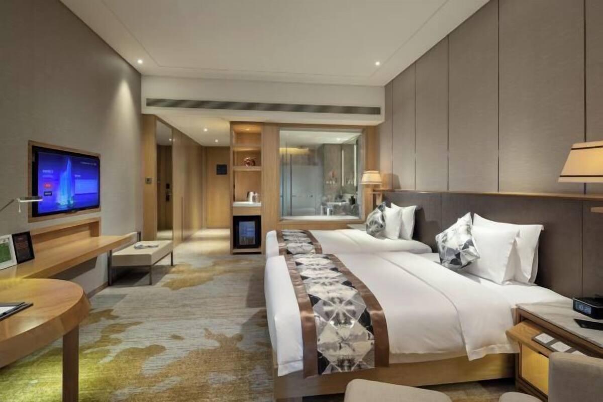 Une chambre d’hôtel équipée d’un lit, d’une télévision, d’un bureau et d’une salle de bain visible à travers une porte en verre.