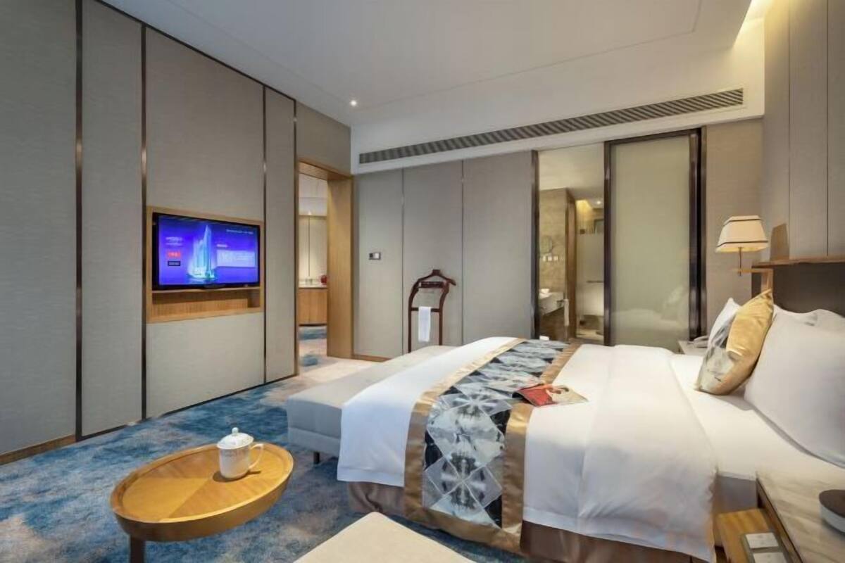Une chambre d’hôtel avec un lit, une télévision, une table de chevet et une petite table en bois sur laquelle se trouve une tasse.