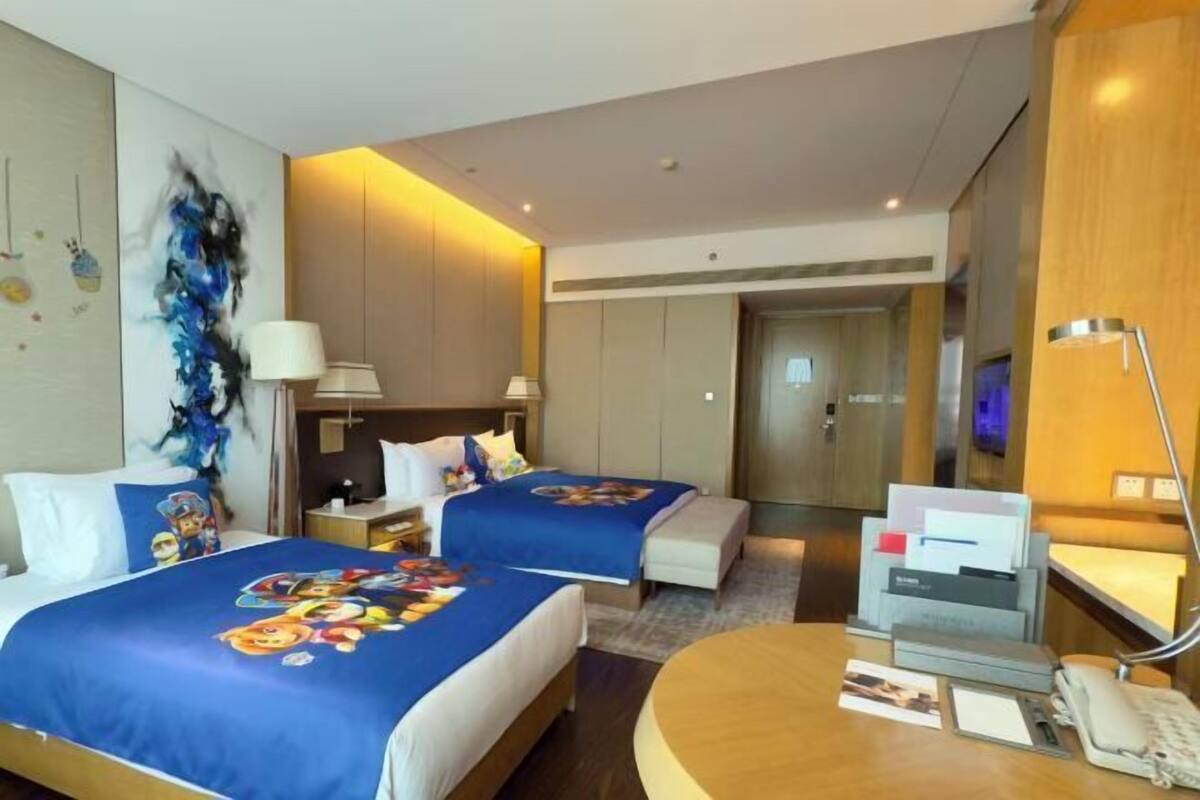 Une chambre d’hôtel avec deux lits, un bureau, une chaise, une télévision et une lampe.