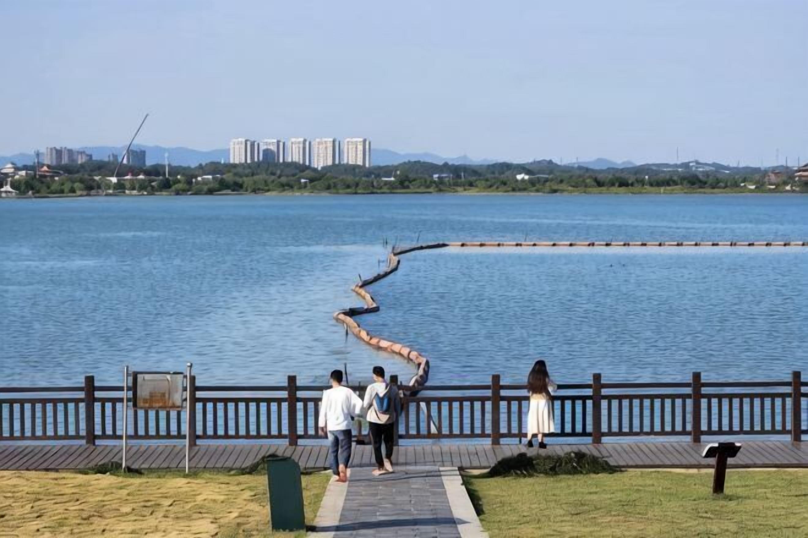 A waterfront park with a wooden walkway, a curved stone barrier, and a distant cityscape.