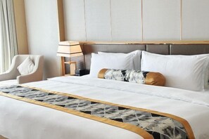 Una cama bien tendida con sábanas blancas y almohadas decorativas, una lámpara de noche y una silla.
