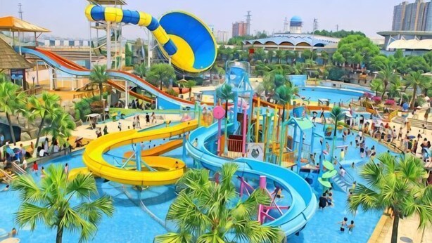 Un parque acuático con toboganes y piscinas, rodeado de palmeras y edificios.