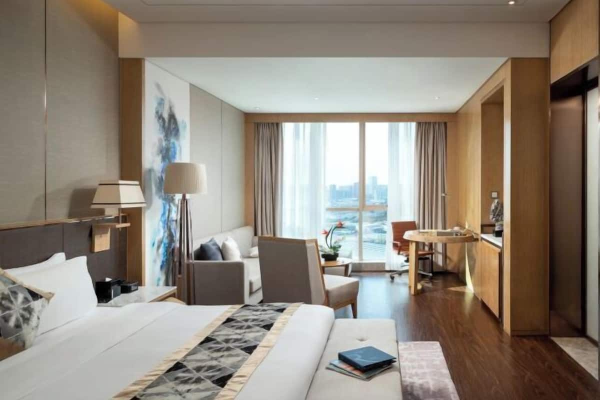 Une chambre d’hôtel avec un lit, un bureau, une chaise, un canapé et une vue sur la ville.