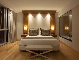 Una habitación de hotel moderna con una cama grande, cabecera de madera, lámparas de noche y un espejo amplio.