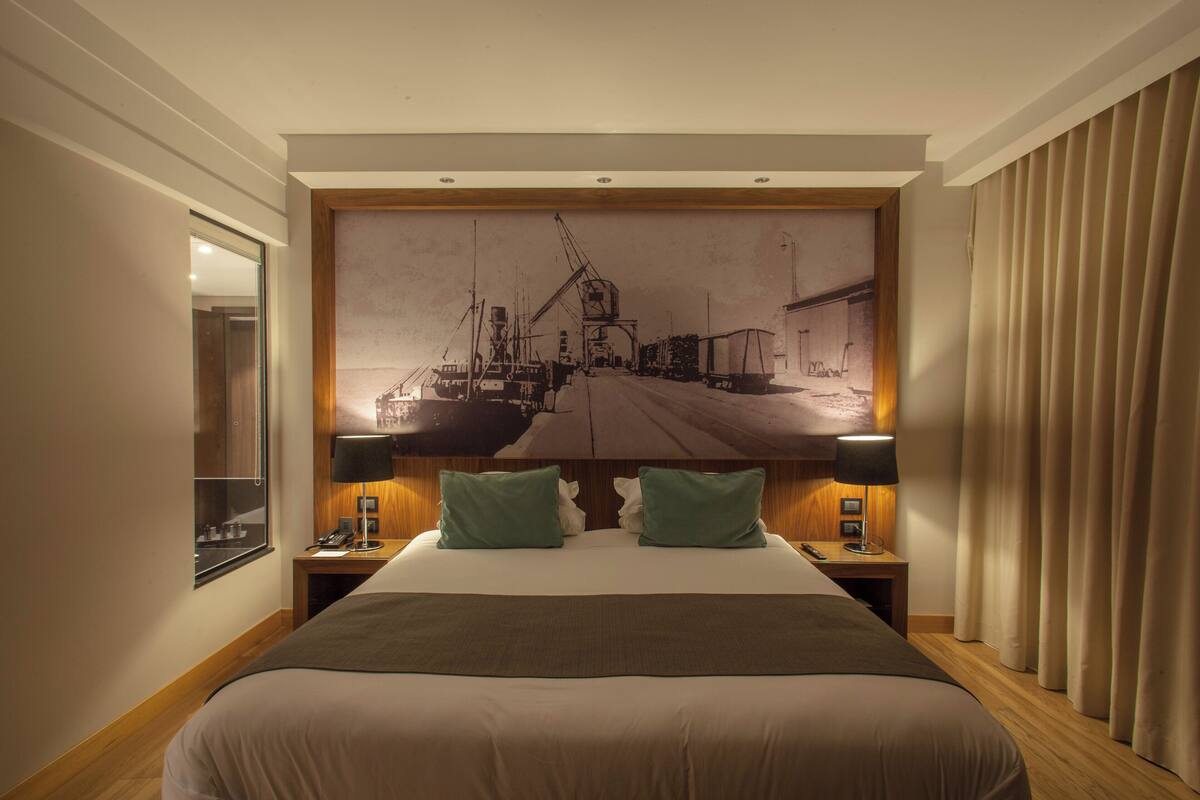 Ein Hotelzimmer mit einem großen Bett, zwei Nachttischen, einem Schminktisch und einem großen Wandbild.