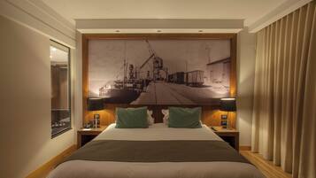 Habitación de hotel con una cama grande, dos mesitas de noche, un tocador, un espejo y un mural grande en la pared.
