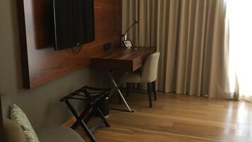 A modern room with a wooden desk, a chair, a television mounted on the wall, and a window with curtains.