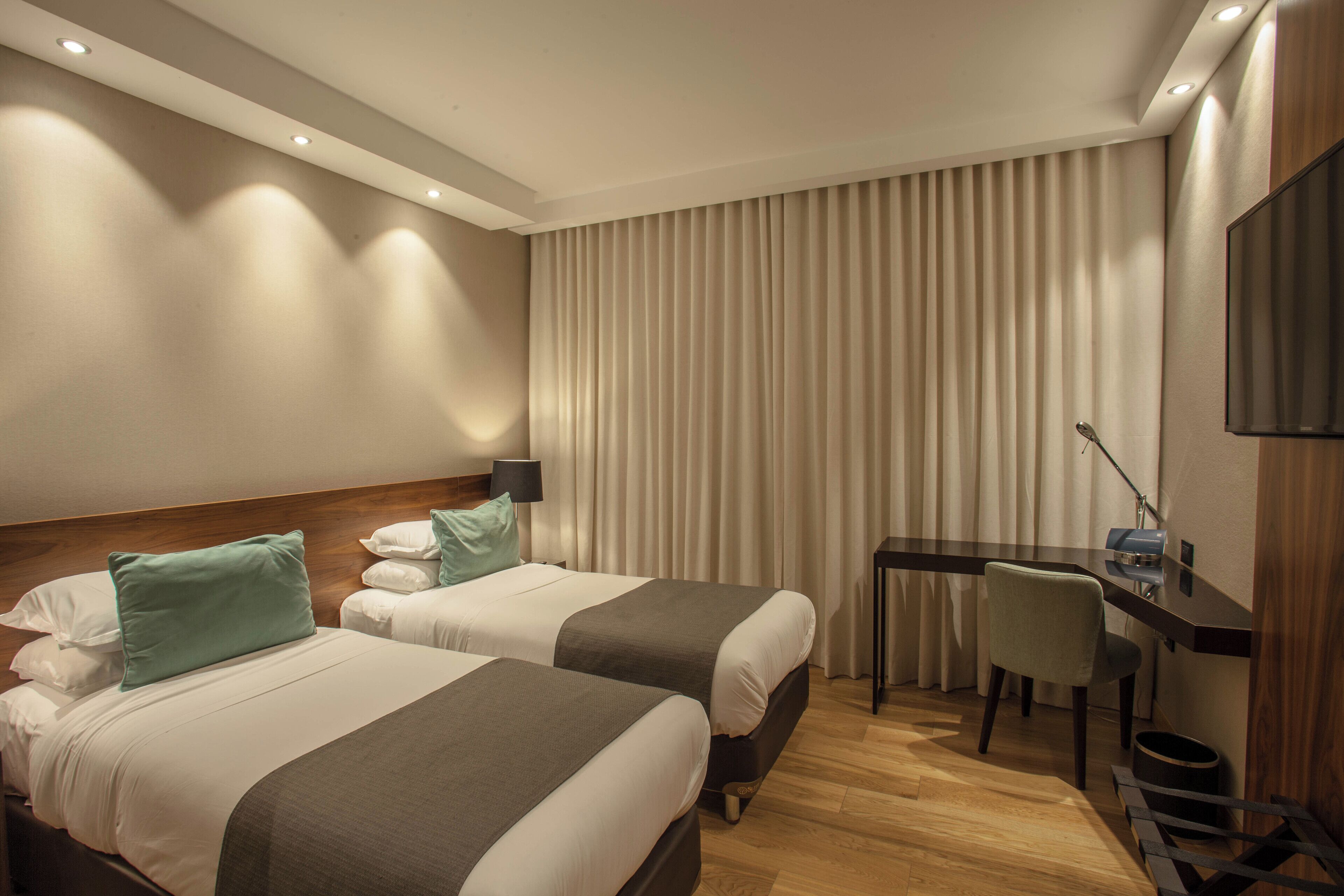 A hotel room with two beds, a desk, a chair, and a TV.