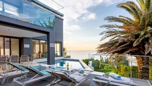 A modern building with a pool area featuring lounge chairs and a glass balustrade overlooking the sea. - Living Hotel Lions Eye (Cape Town)