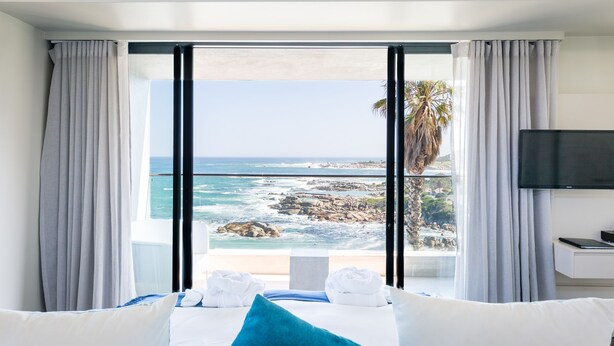 A hotel room with a large window offering a view of the ocean and rocky coastline. - Living Hotel Lions Eye (Cape Town)