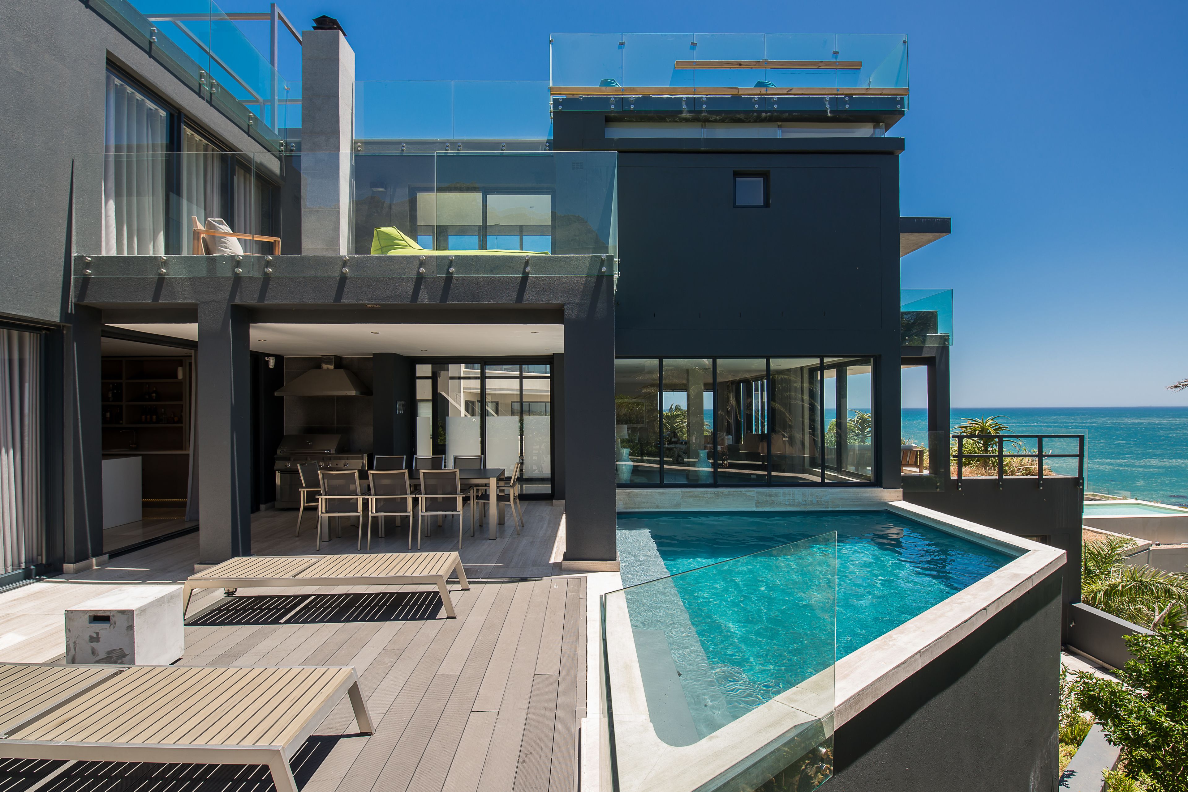 A modern house with a rooftop pool, outdoor seating, and a view of the ocean.