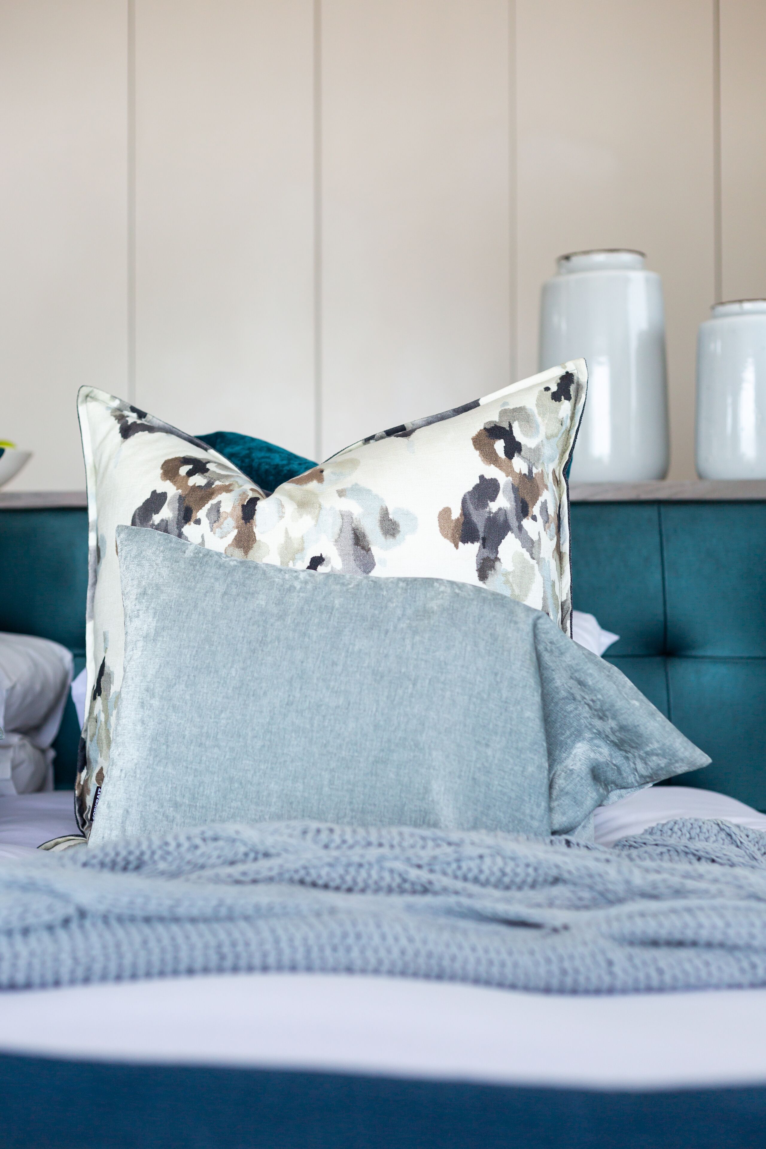 Un lit avec une tête de lit bleue, un oreiller gris et un coussin à motifs floraux.