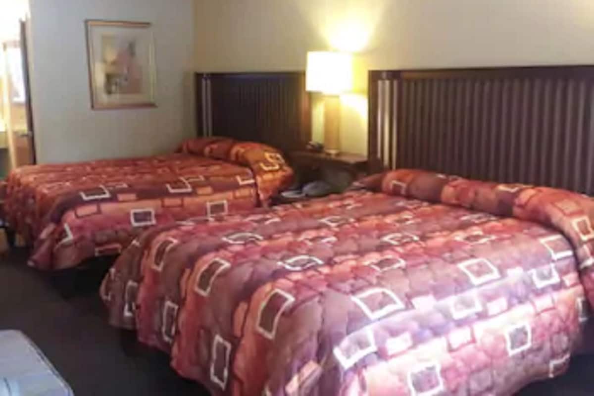A hotel room with two beds, a nightstand, a lamp, and a painting on the wall.