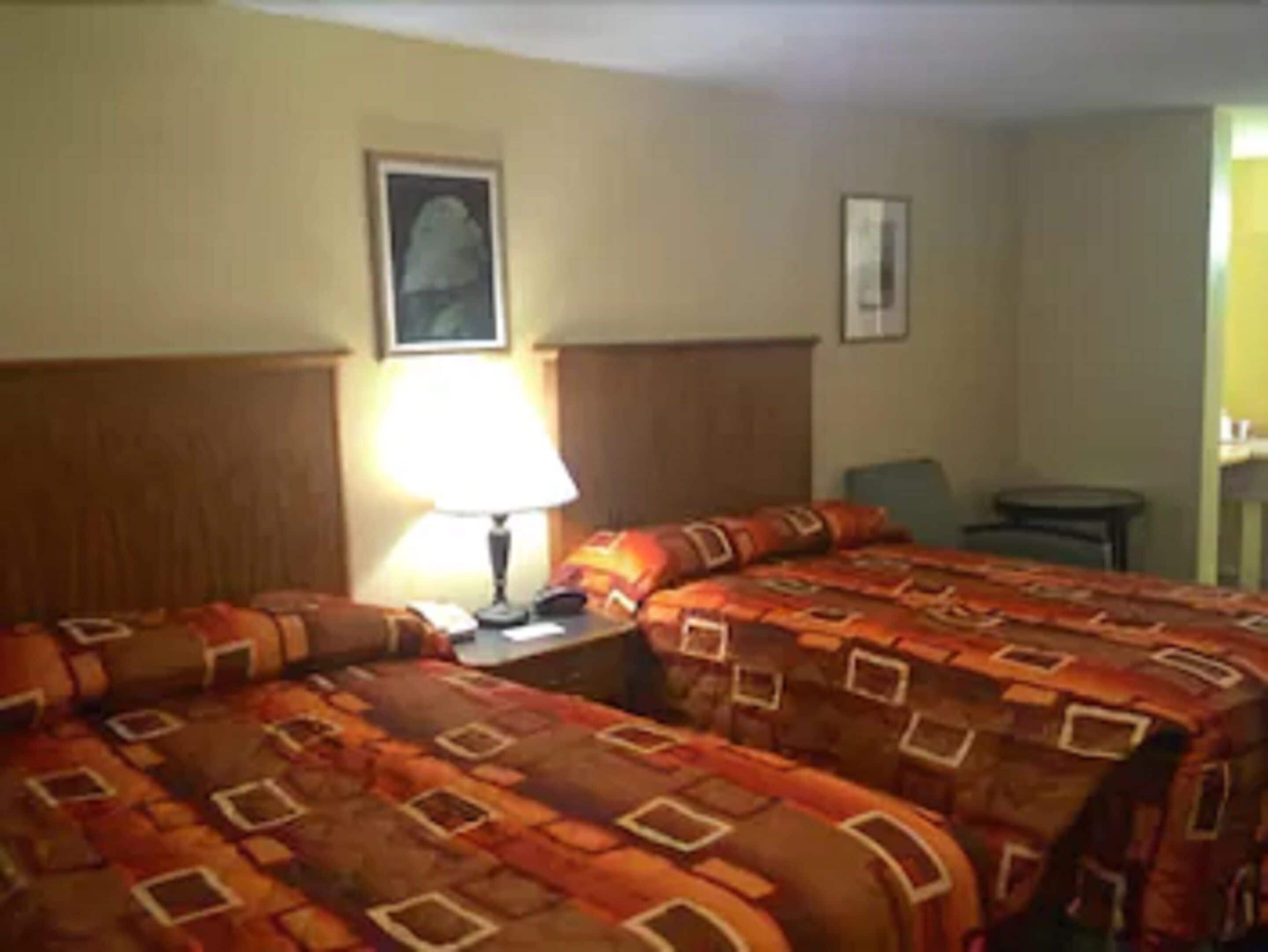 Ein Hotelzimmer mit zwei Betten, einem Nachttisch mit Lampe, einem Sessel und einem kleinen Tisch.