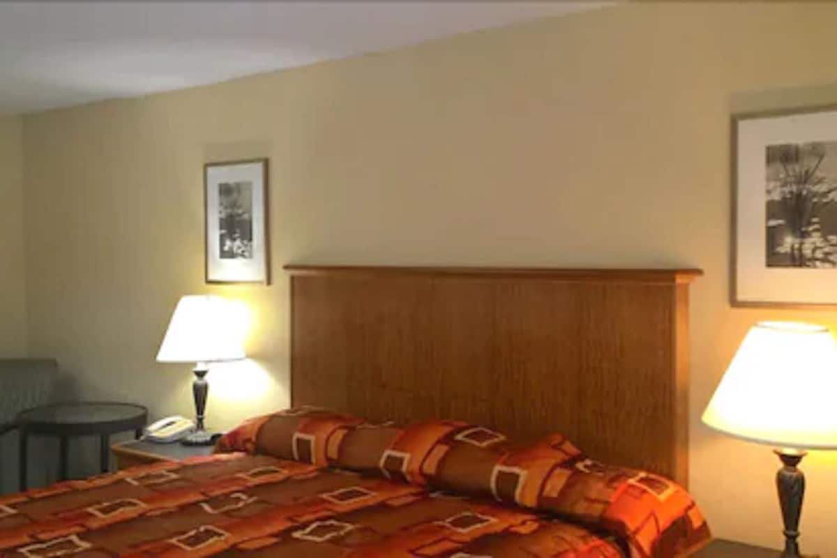 A hotel room with a bed, two bedside lamps, a chair, a small table, and two framed pictures on the wall.