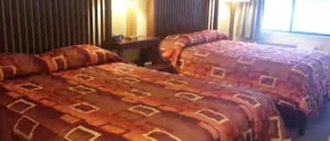 A hotel room with two beds, a nightstand, and a window with curtains.