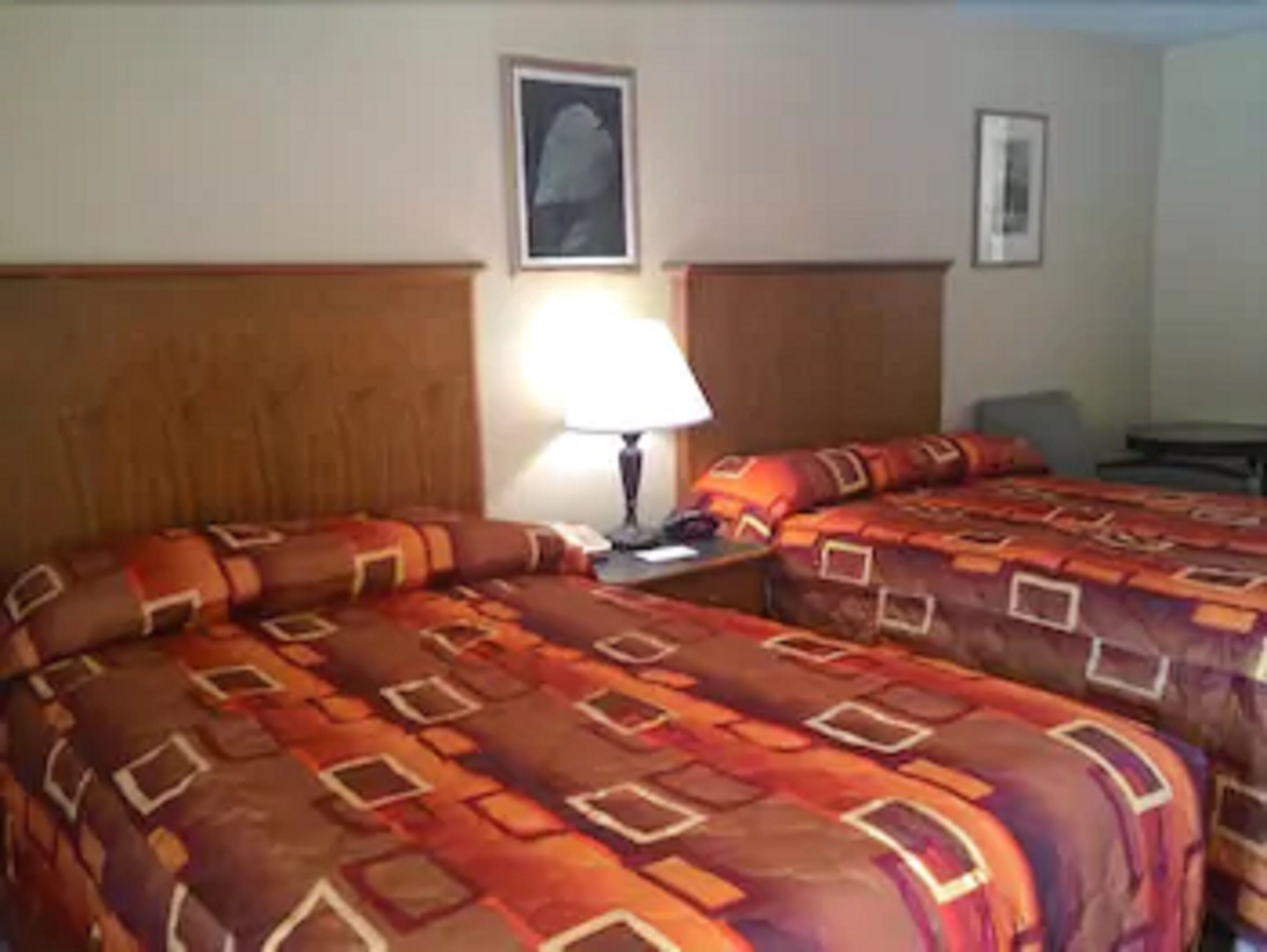 Habitación de hotel con dos camas, una mesita de noche, una lámpara y un cuadro en la pared.