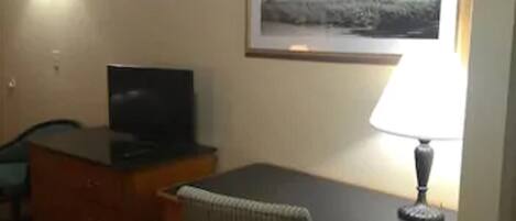 Een hotelkamer met een bureau, stoel, televisie, lamp en een ingelijst schilderij aan de muur.