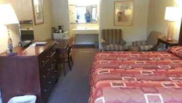 A hotel room with a bed, a desk, a chair, a dresser, a lamp, and a mirror.