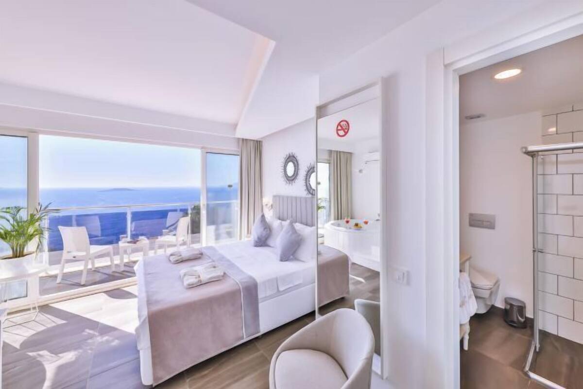A modern hotel room with a balcony, a bed, a desk, and a bathroom.
