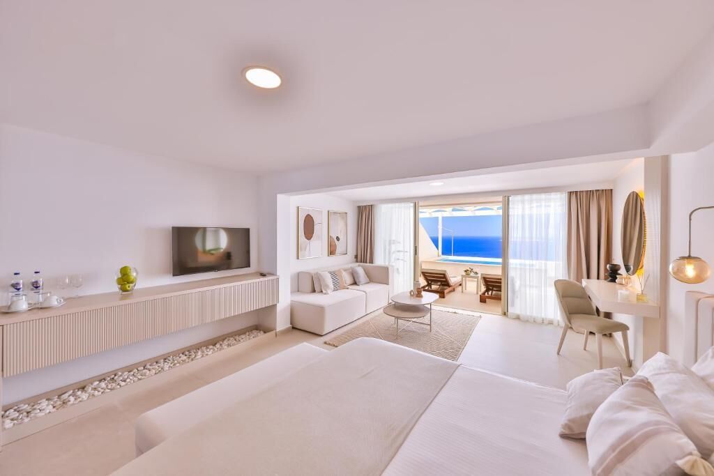 Et moderne hotelværelse med en stor seng, en sofa, et spiseområde med havudsigt og et fjernsyn på væggen.
