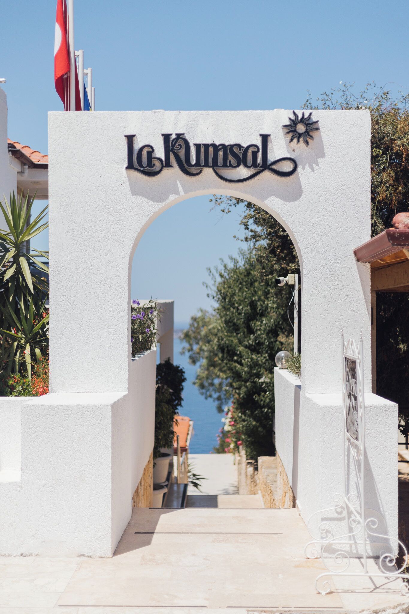 An entrance archway with the sign "La Kunsal" and a clear view of the sky and greenery beyond.