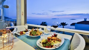 Una mesa dispuesta con platos de comida y copas de vino, con vistas a un paisaje marino y a las islas.