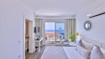 Habitación de hotel con una cama grande, un escritorio con televisor, un balcón con vista al mar y una planta en maceta.