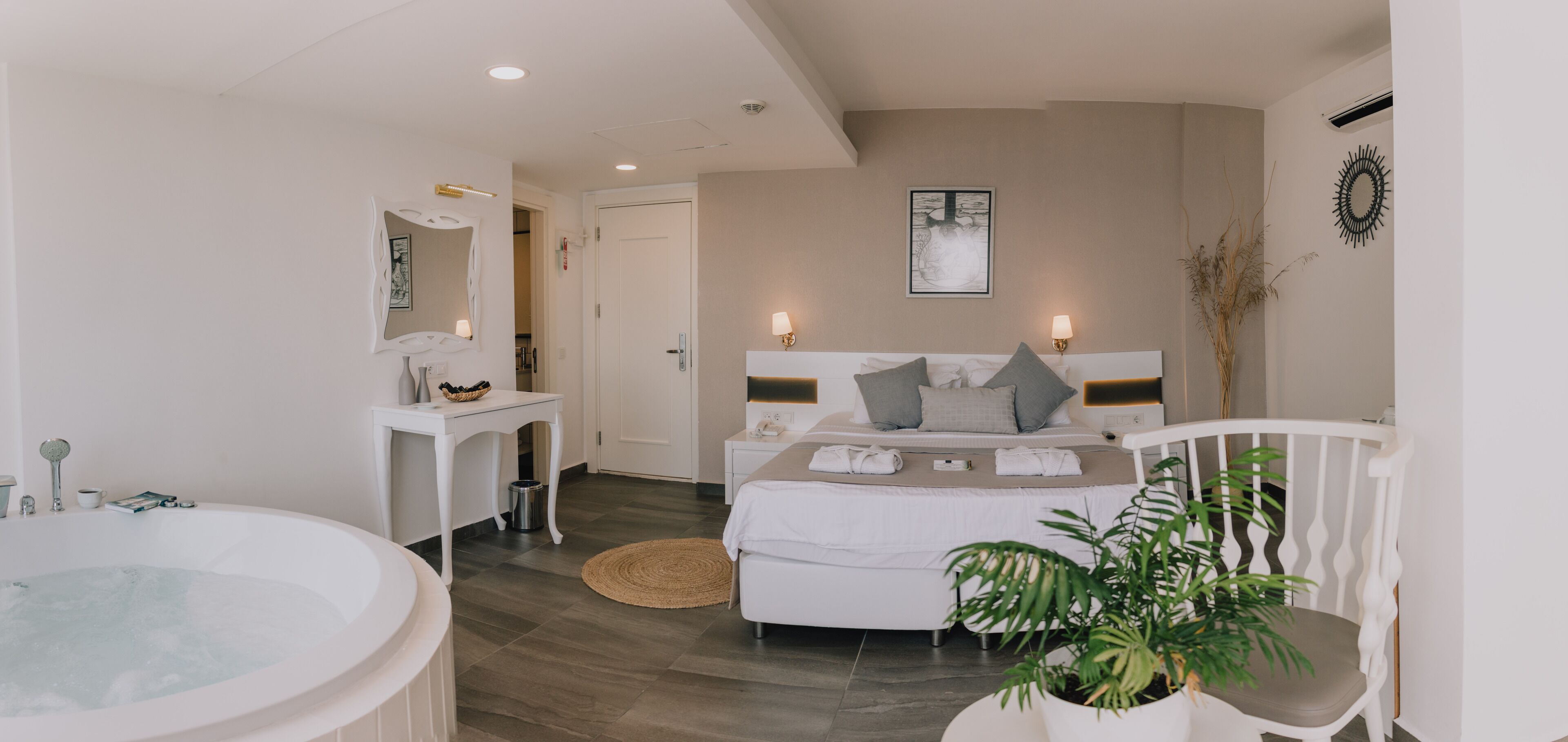 A modern bedroom with a large bed, bedside tables, a bathtub, and a potted plant.
